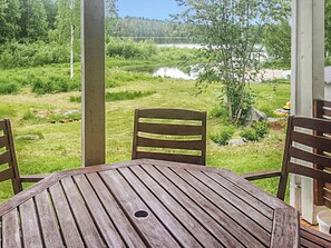 Une terrasse extérieure avec une table et des chaises en bois, donnant sur un espace verdoyant agrémenté d’arbres et d’une étendue d’eau.