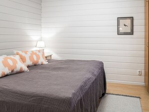 Ein Schlafzimmer mit Bett, Kissen, einem Nachttisch, einer Lampe und einem gerahmten Bild an der Wand.