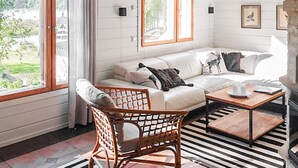 Un salon chaleureux avec un canapé blanc, un fauteuil en osier, une table basse et une cheminée.