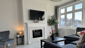 Un salon moderne doté d’une cheminée, d’un téléviseur à écran plat et offrant une vue sur la ville grâce à de grandes fenêtres.