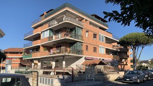 Un immeuble à plusieurs étages doté de balcons, d’un commerce au rez-de-chaussée et de voitures garées.