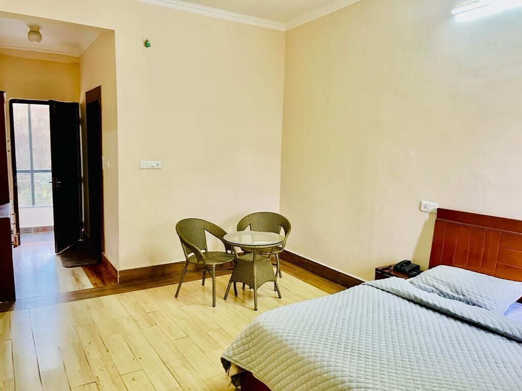 A hotel room with a bed, a small table with chairs, and a view of the outside.