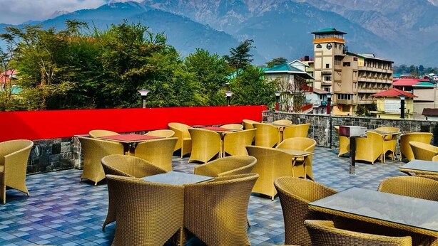 An outdoor seating area with wicker furniture and a view of mountains in the background. - Hotel Suryadev (Palampur)