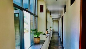 A long, narrow hallway with large windows on one side and a tiled floor. - Hotel Suryadev (Palampur)