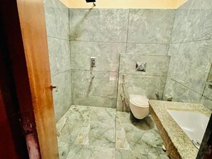A bathroom with a marble floor, a toilet, a sink, and a shower. - Hotel Suryadev (Palampur)
