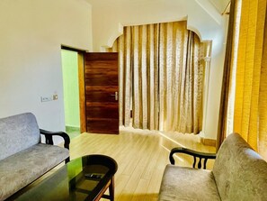 A living room with a wooden door, a sofa, a coffee table, and a curtain. - Hotel Suryadev (Palampur)