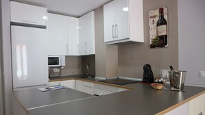 A modern kitchen with white cabinets, a microwave, a coffee maker, and a wine bottle on the counter. - Apartamento Premium un Dormitorio con Terraza (Fuengirola)
