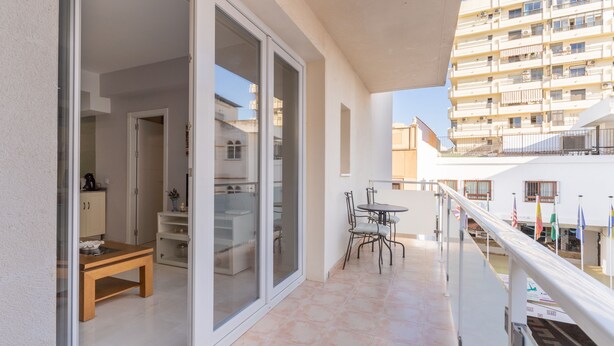 A balcony with a dining table and chairs, a sliding glass door leading to a kitchen, and a view of a multi-story building. - Apartamento Premium un Dormitorio con Terraza (Fuengirola)