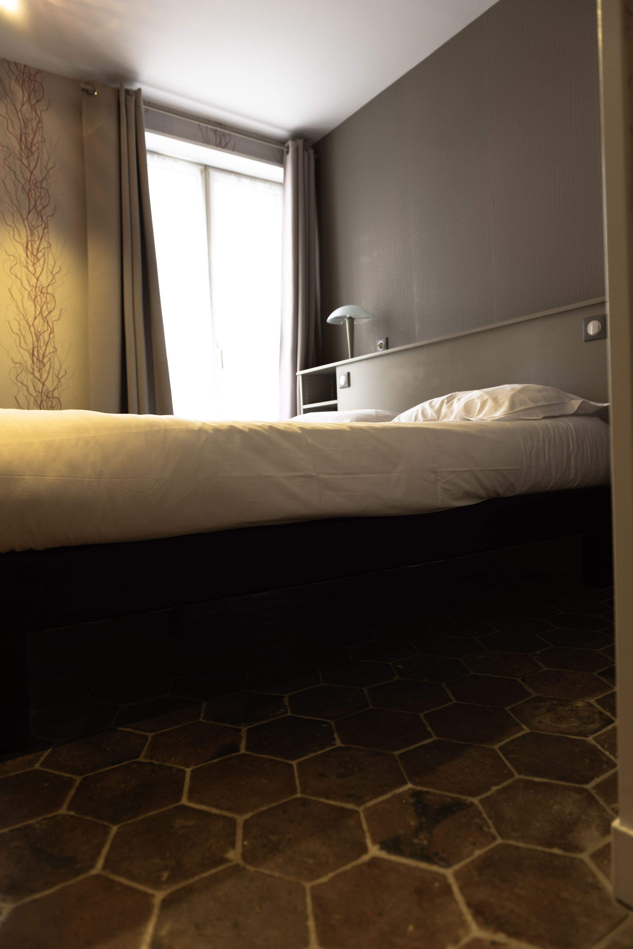 Uma cama de solteiro com cabeceira, mesa de cabeceira e janela com cortinas.