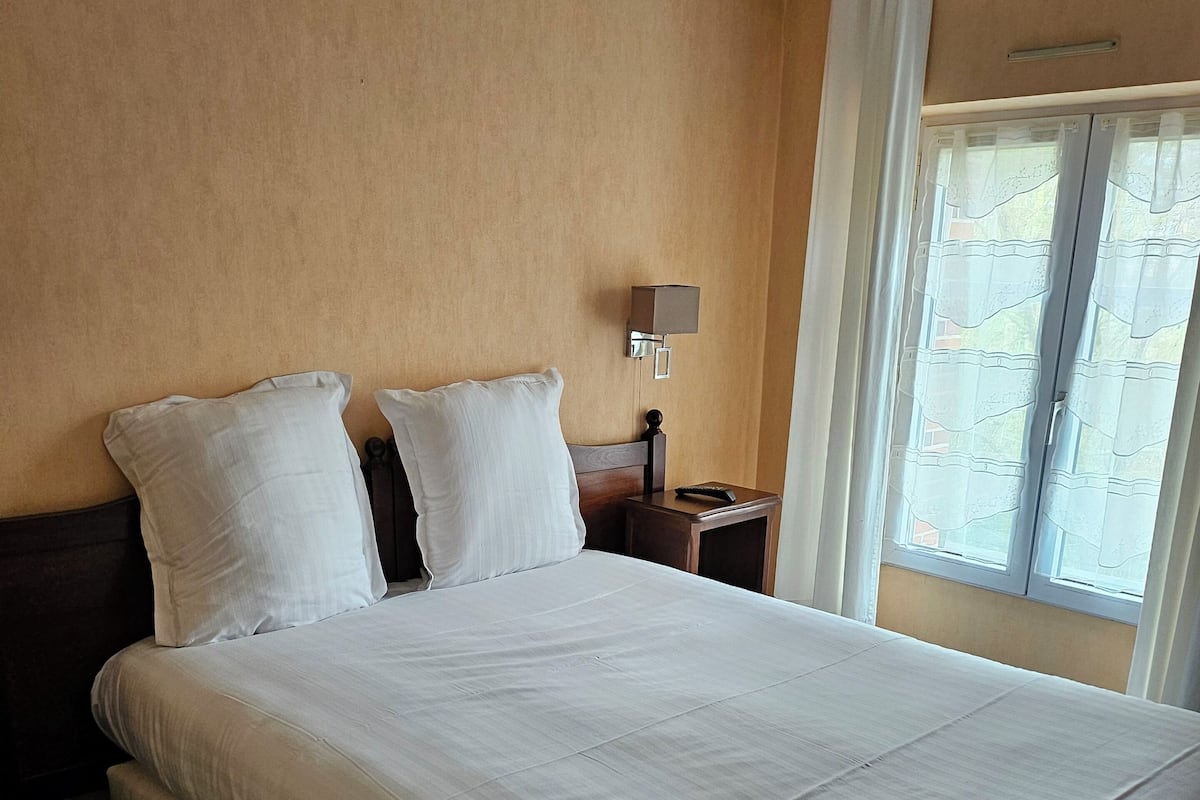 Une chambre d’hôtel avec un grand lit, une table de chevet avec une lampe et une fenêtre avec des rideaux.