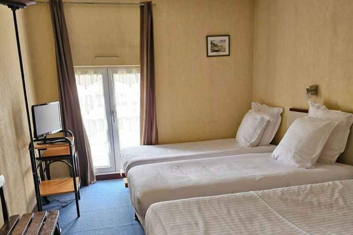 Une chambre d’hôtel avec deux lits, un bureau, une chaise et une fenêtre avec des rideaux.