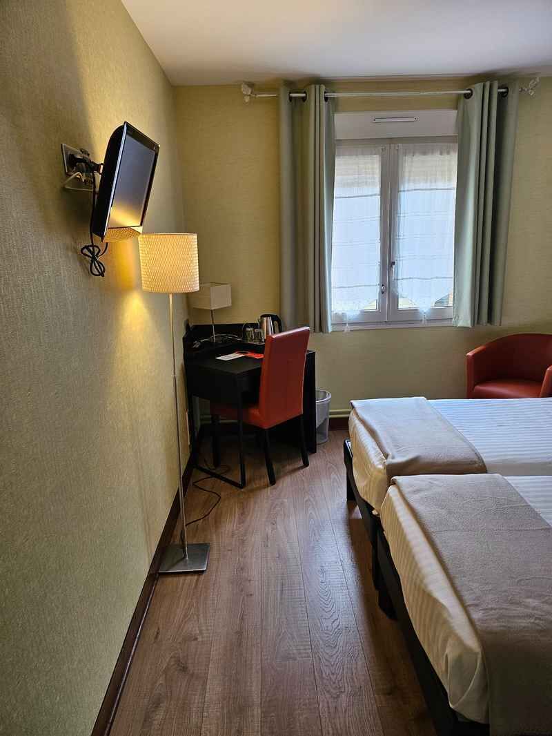 A hotel room with a desk, two beds, a TV, and a window with curtains.