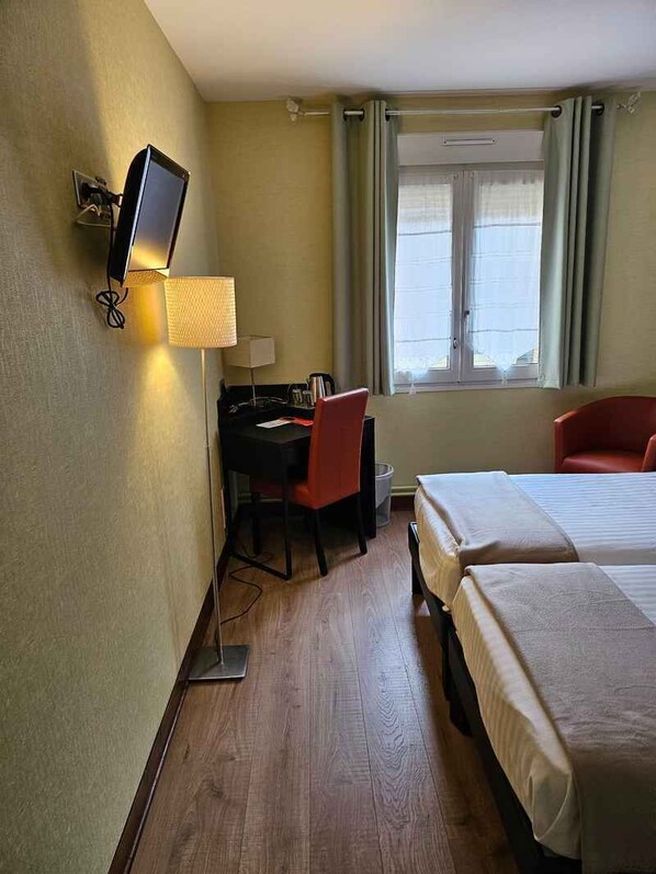 Una habitación de hotel con escritorio, dos camas, televisor y ventana con cortinas.