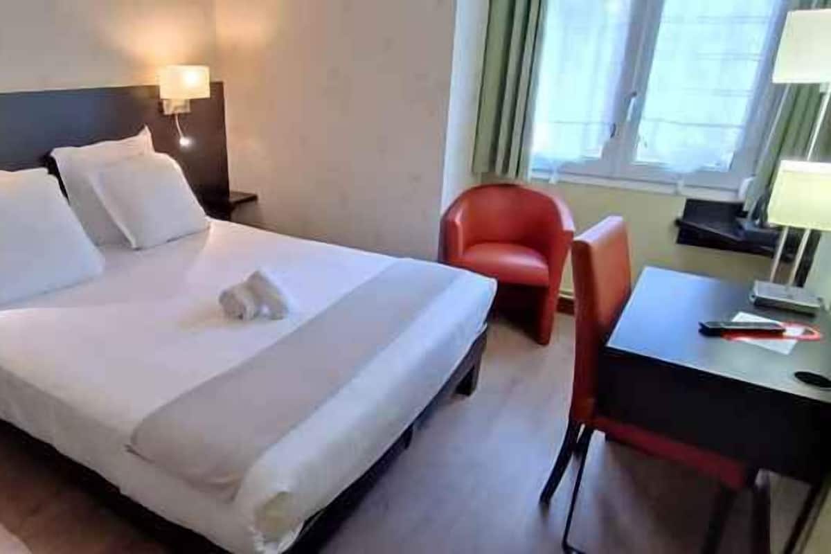 Une chambre d’hôtel avec un lit, deux tables de chevet, un bureau, une chaise et une fenêtre.