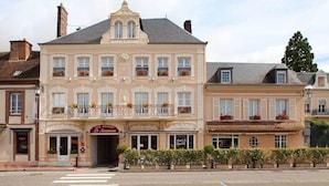 Un bâtiment historique doté d’une entrée centrale, d’un balcon orné de jardinières et d’une enseigne indiquant qu’il s’agit d’un hôtel et d’un restaurant.