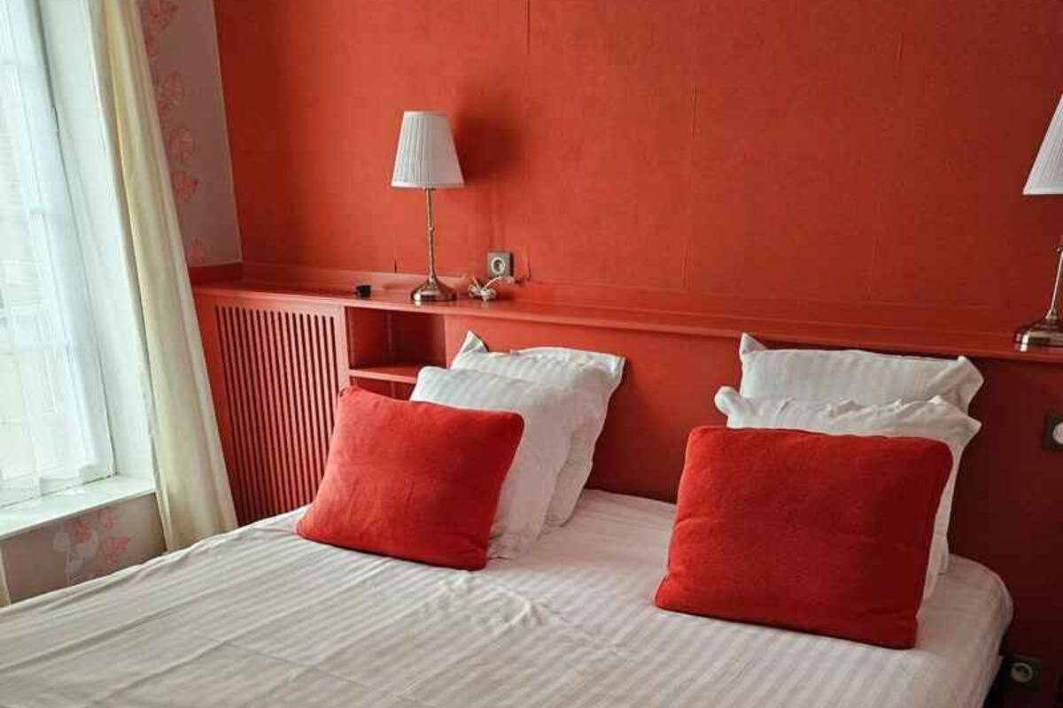 Une chambre d’hôtel avec un grand lit, deux tables de chevet, une fenêtre avec des rideaux et un mur d’accent de couleur rouge.