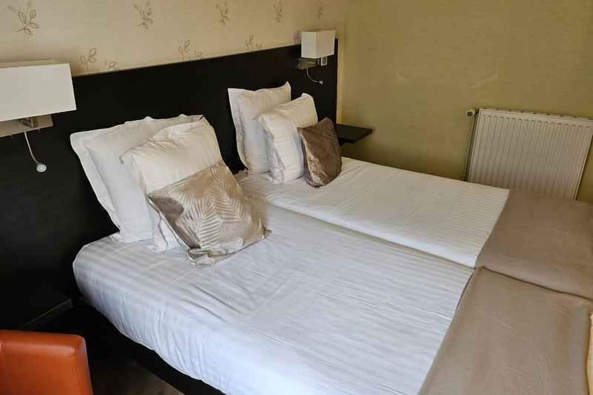 Une chambre d’hôtel avec deux lits, une table de chevet, une lampe et un radiateur.