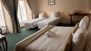 Une chambre d’hôtel avec deux lits simples, un grand lit, une table en bois et un lustre.
