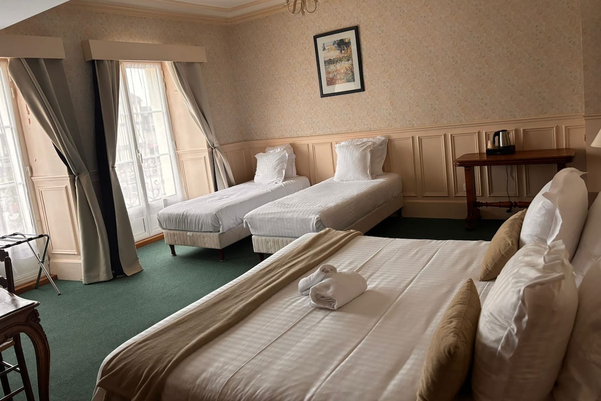 Une chambre d’hôtel avec deux lits simples, un grand lit, une table en bois et un lustre.