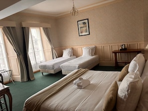 Habitación de hotel con dos camas individuales, una cama grande, una mesa de madera y un candelabro.