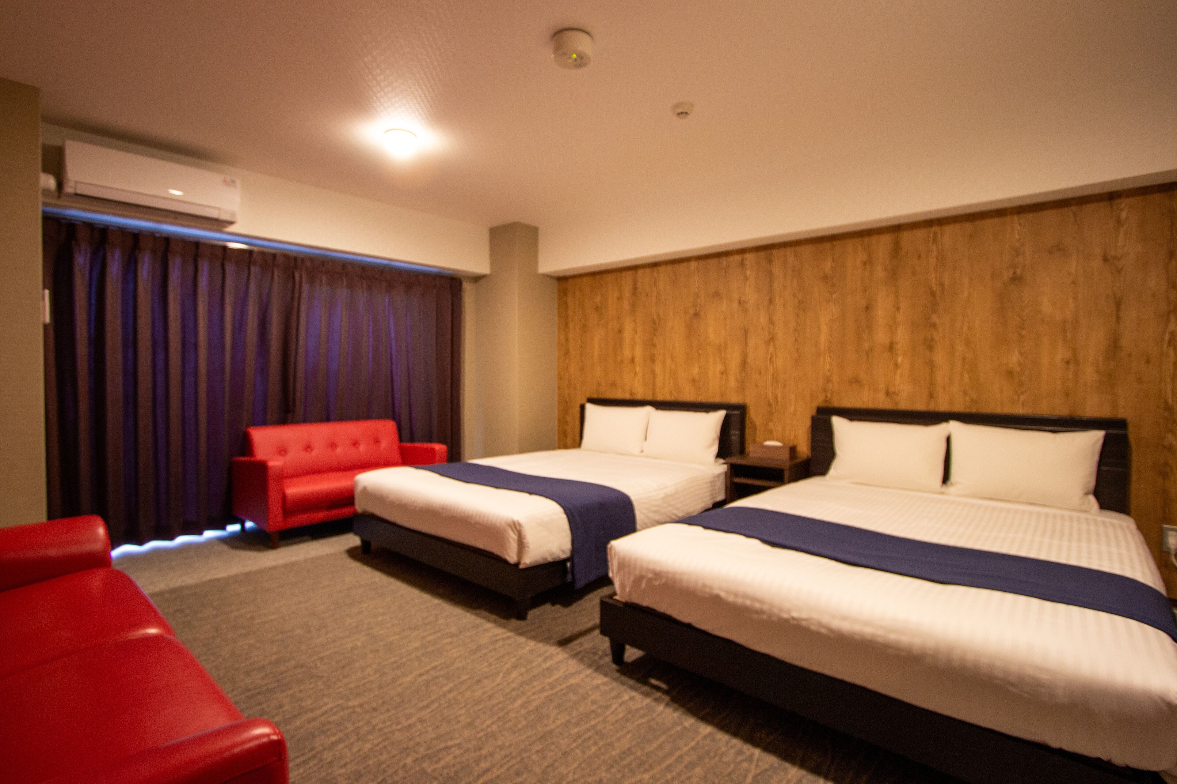 A hotel room with two beds, a red sofa, and a wooden panel wall.