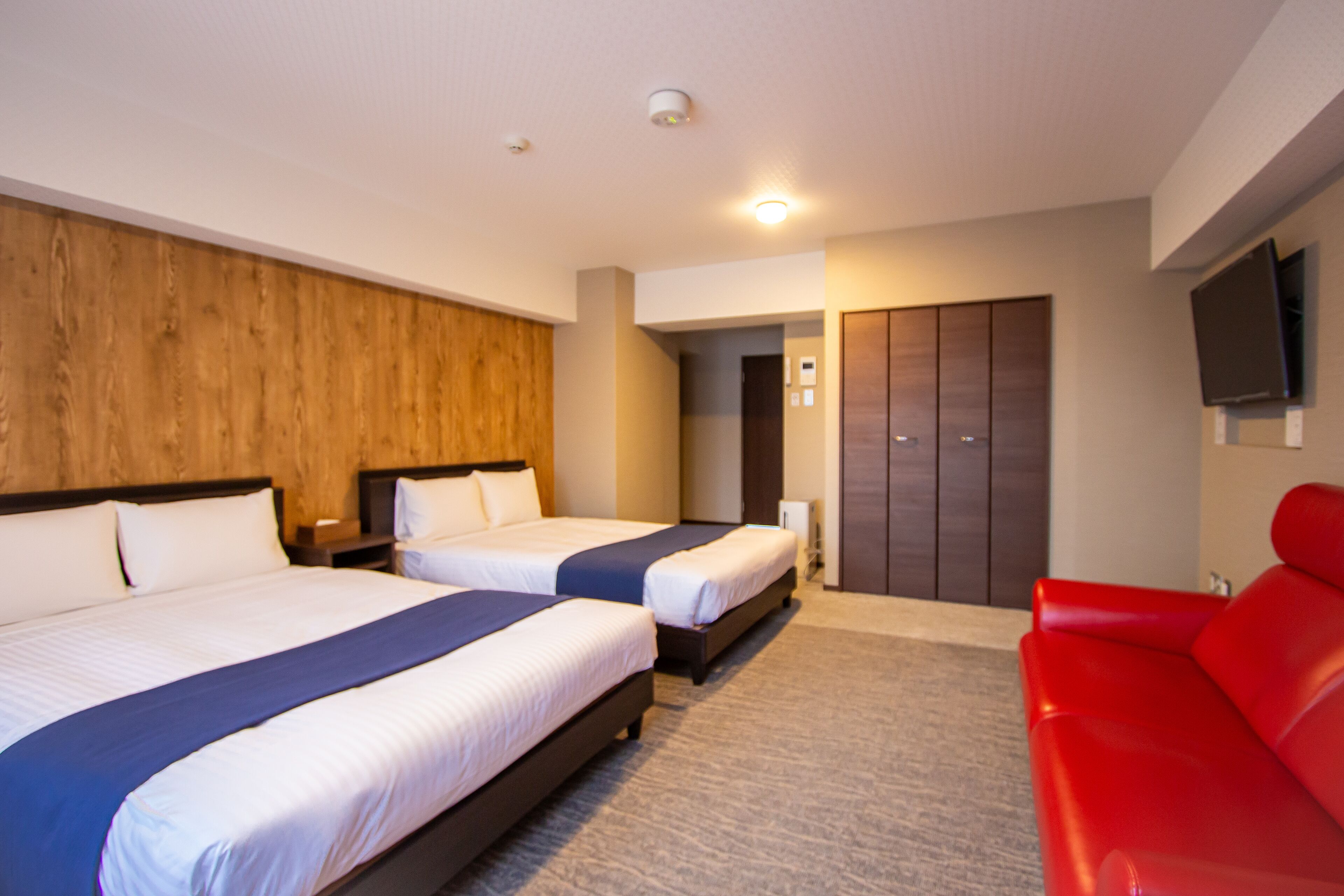 Habitación de hotel con dos camas, un sofá rojo, un televisor y un armario.