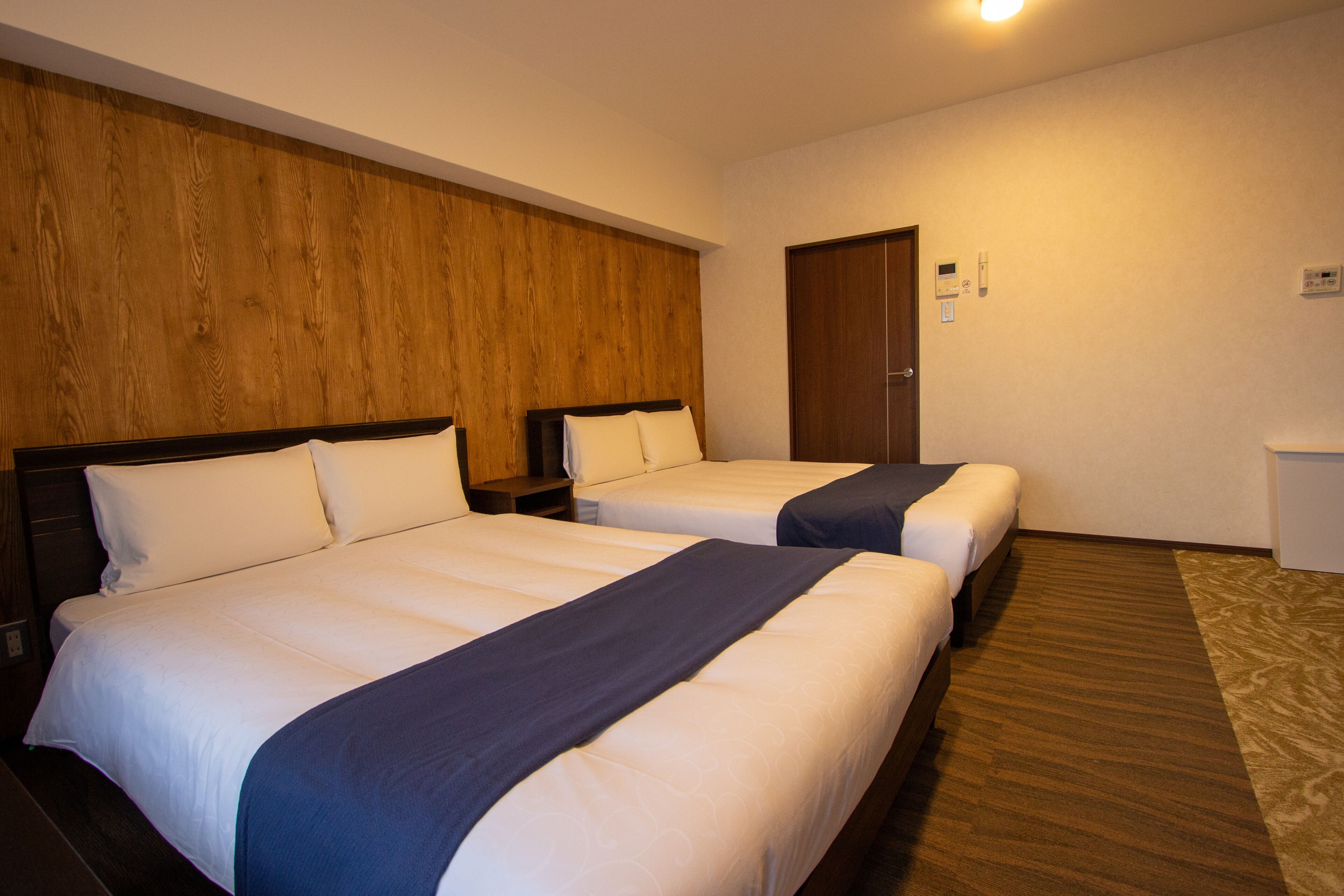 Una habitación de hotel con dos camas, cabecero de madera, una puerta y un pequeño escritorio.