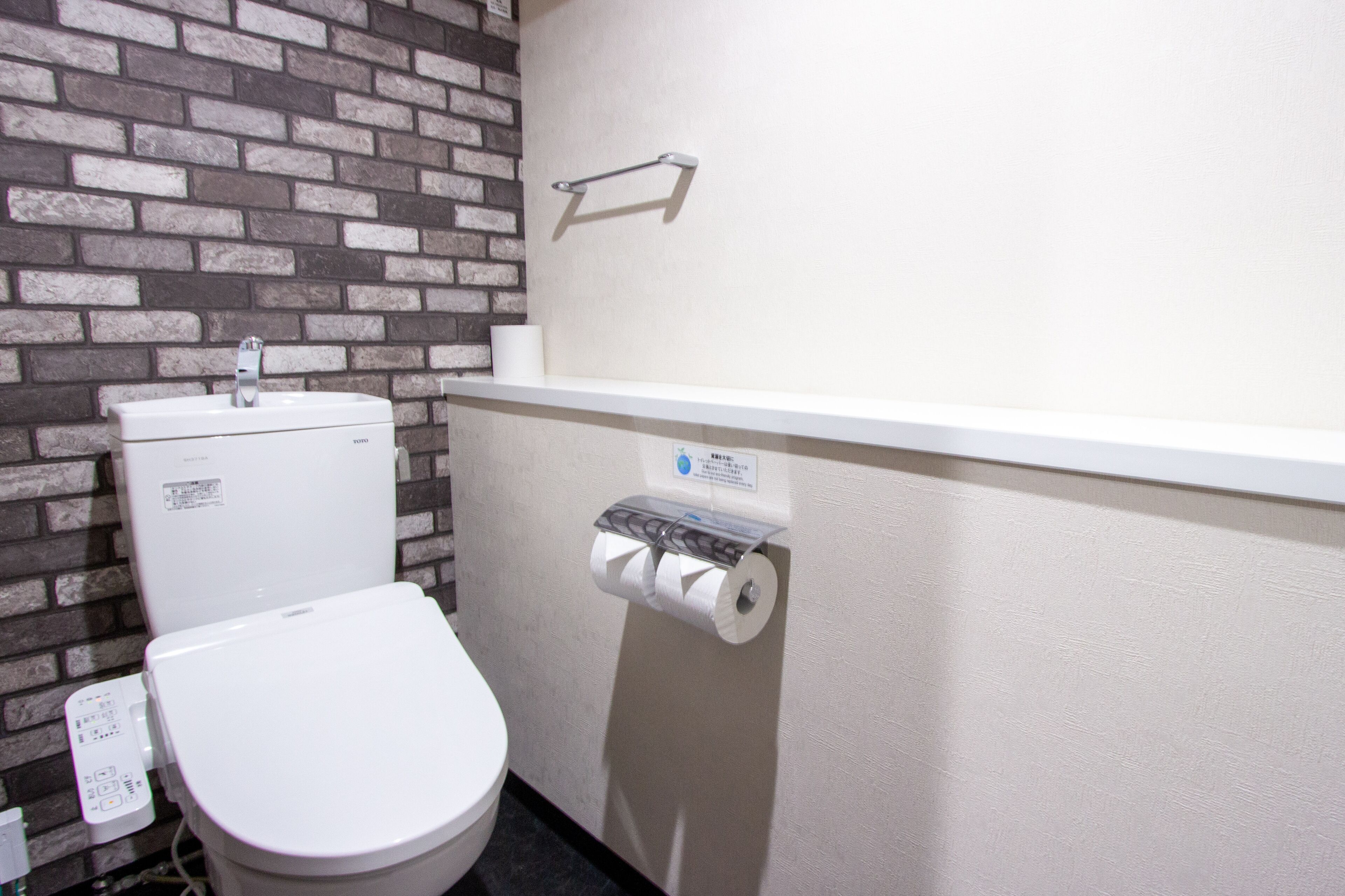 Une salle de bain avec des toilettes blanches, un lavabo blanc et un porte-rouleau de papier toilette fixé au mur.