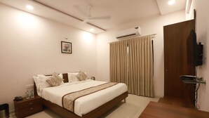 A hotel room with a large bed, a TV mounted on the wall, and a curtain on the window. - Chandanvan Club & Resort (Navsari)