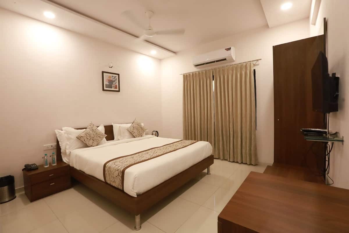 A hotel room with a large bed, a TV mounted on the wall, and a curtain on the window.