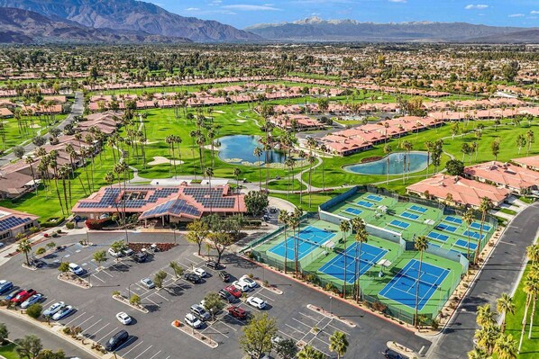 Um campo de golfe com vários campos de tênis, um parque de estacionamento e um edifício com painéis solares.