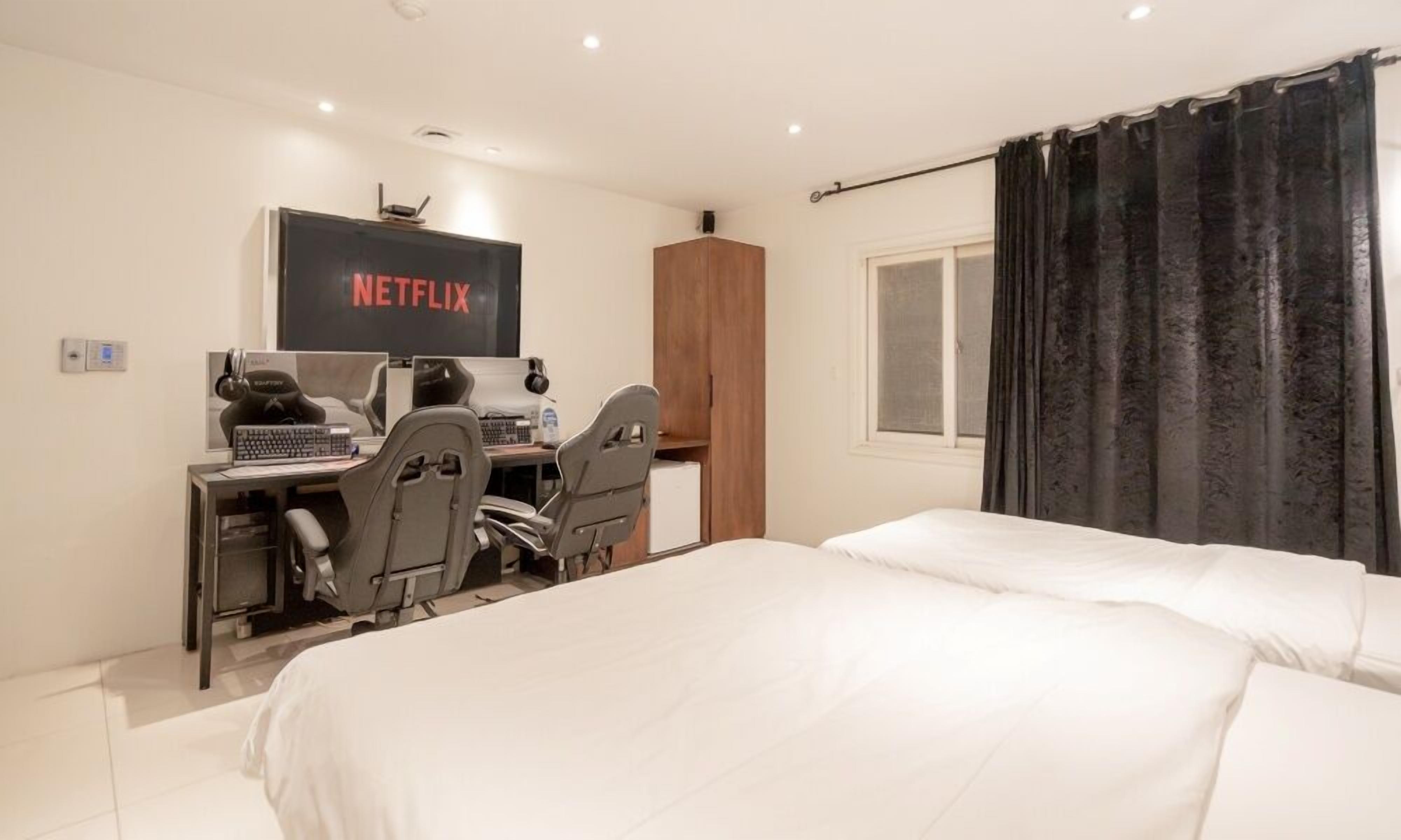 A bedroom with a bed, a desk with a computer, a chair, a wardrobe, and a window with curtains.