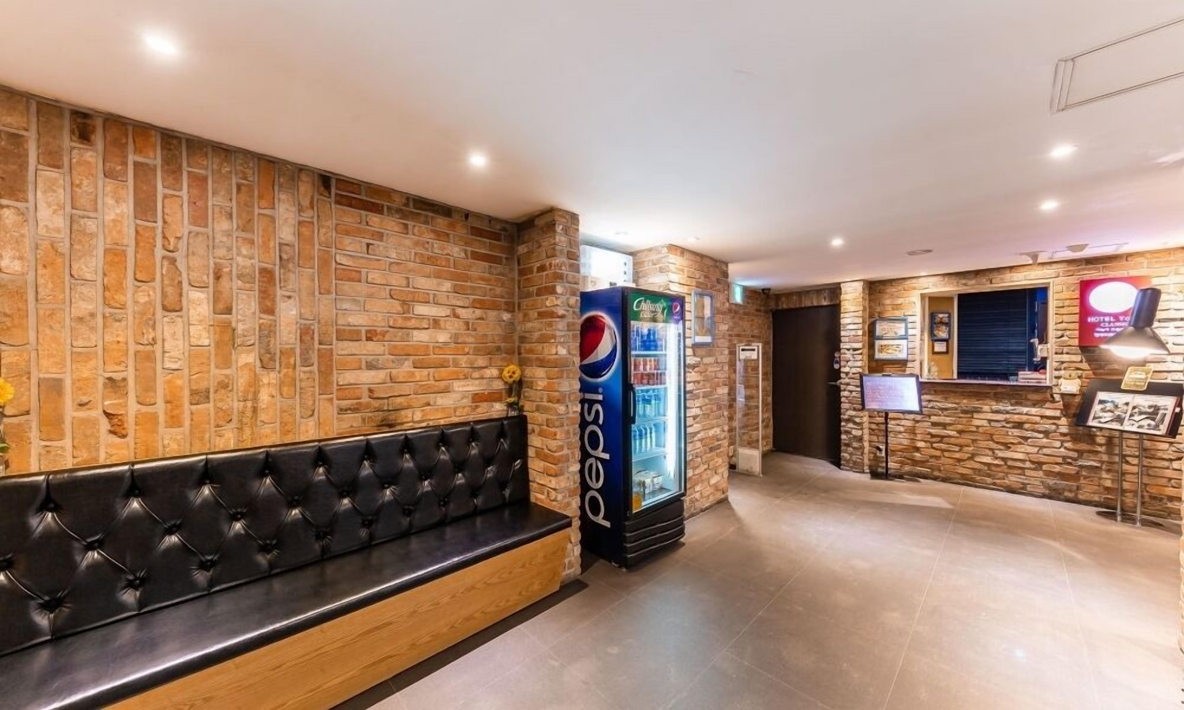 Un vestíbulo con pared de piedra, un banco de cuero negro, un refrigerador de Pepsi y un mostrador de recepción.