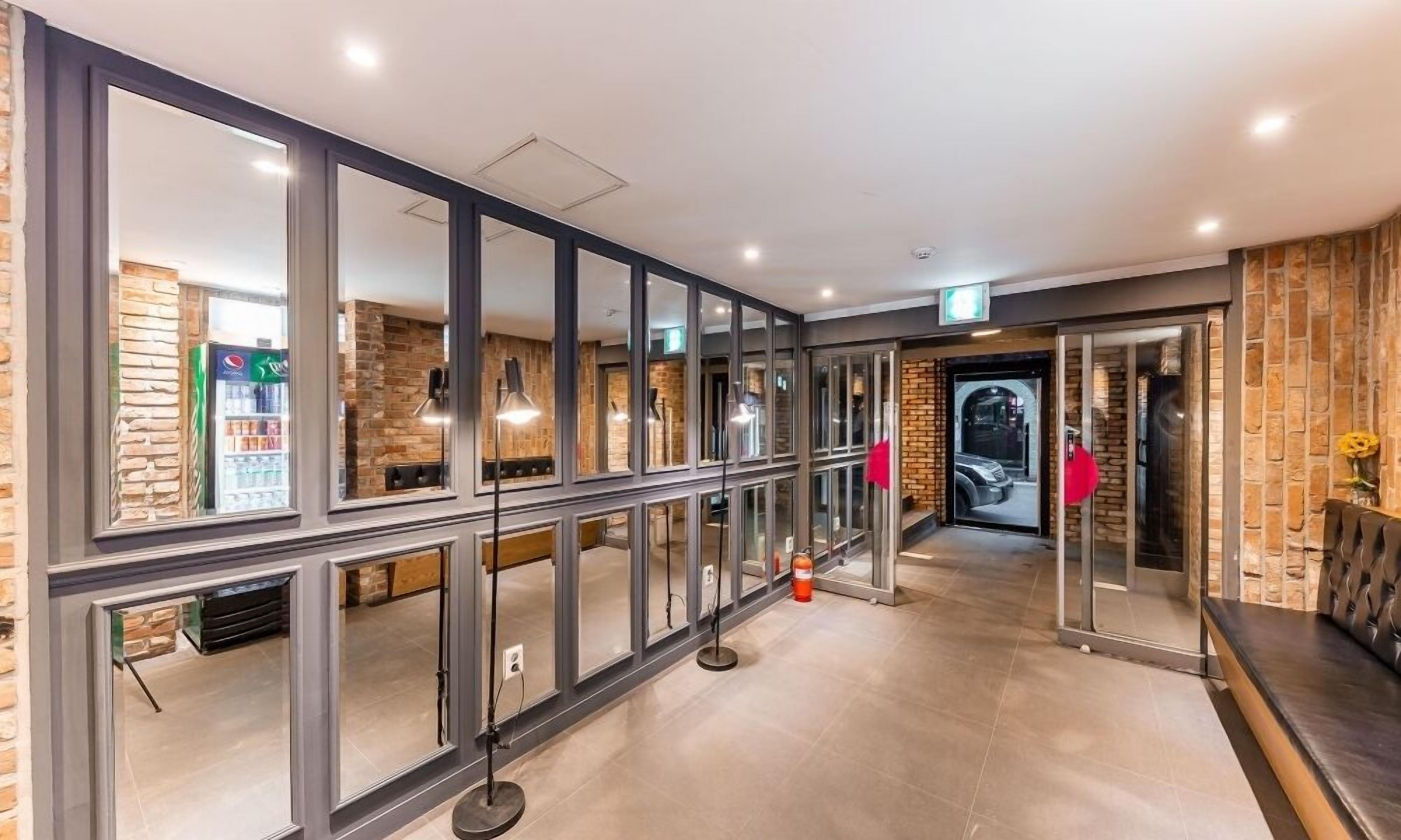 A modern hotel lobby with glass doors, a seating area, and a visible fire extinguisher.