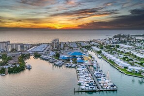 Un port de plaisance avec des bateaux amarrés, un bâtiment au toit bleu et un coucher de soleil sur l’eau.