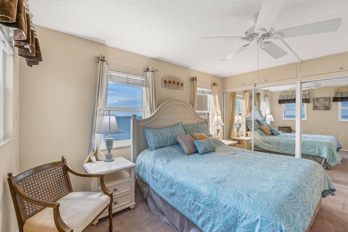 A bedroom with a bed, a chair, a nightstand, a mirror, and a ceiling fan.