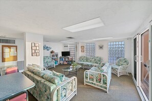 A cozy living room with a sofa, a small table, and a television. There is a window with decorative glass panels and a bulletin board on the wall. - Expansive Gulf Views from Balcony | San Marco on Venice with Private Beach | Heated Pool | King Bed (Venice)