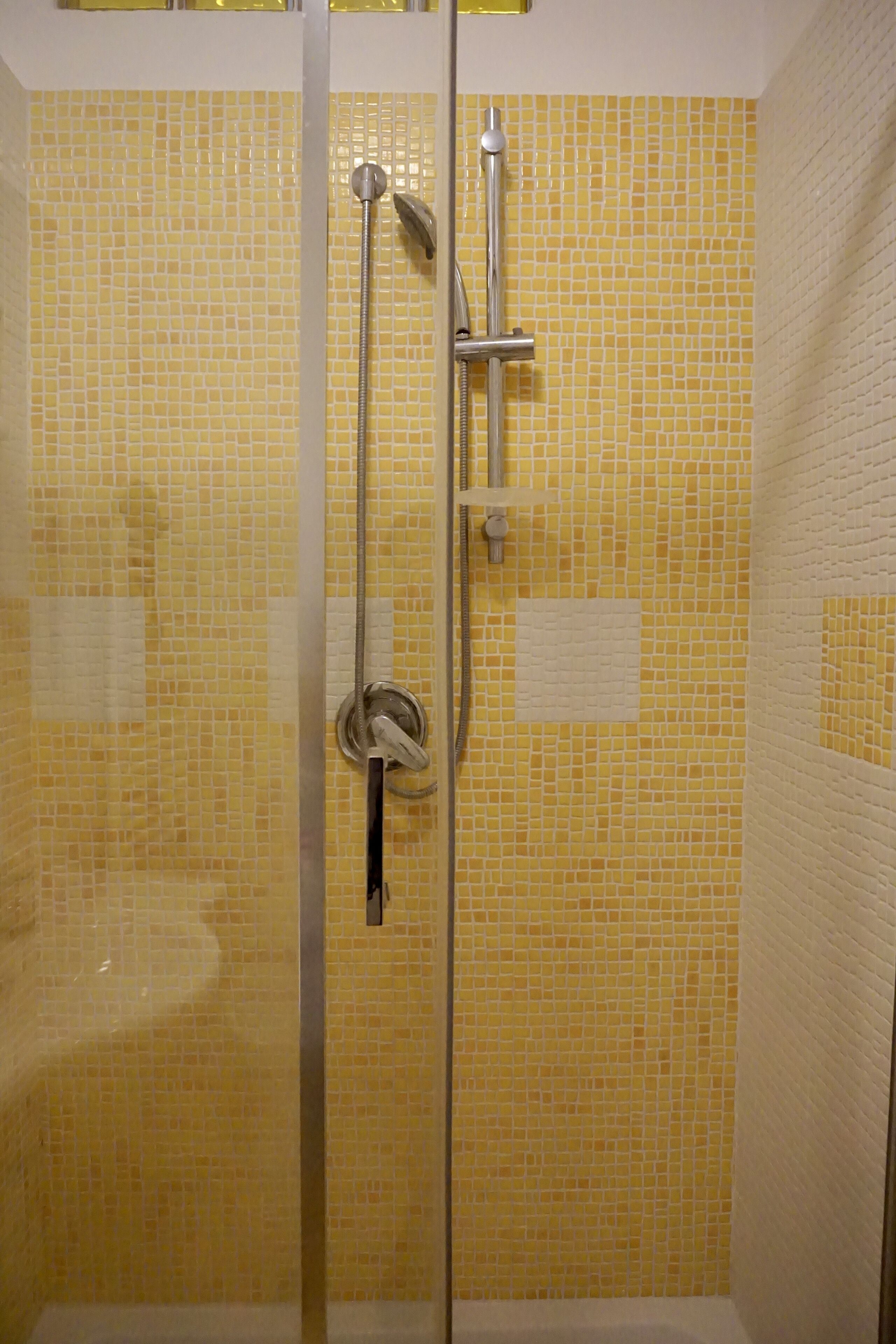 Cabina doccia in vetro con parete rivestita di piastrelle gialle e soffione cromato.