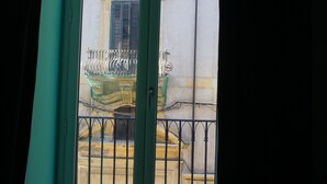 Vista attraverso una porta di vetro con ringhiera metallica, che si apre su un balcone con balaustra.
