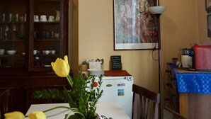 Un'area pranzo con un tavolo apparecchiato per quattro persone, un vaso di tulipani gialli, un quadro incorniciato e un mobile con ante in vetro.