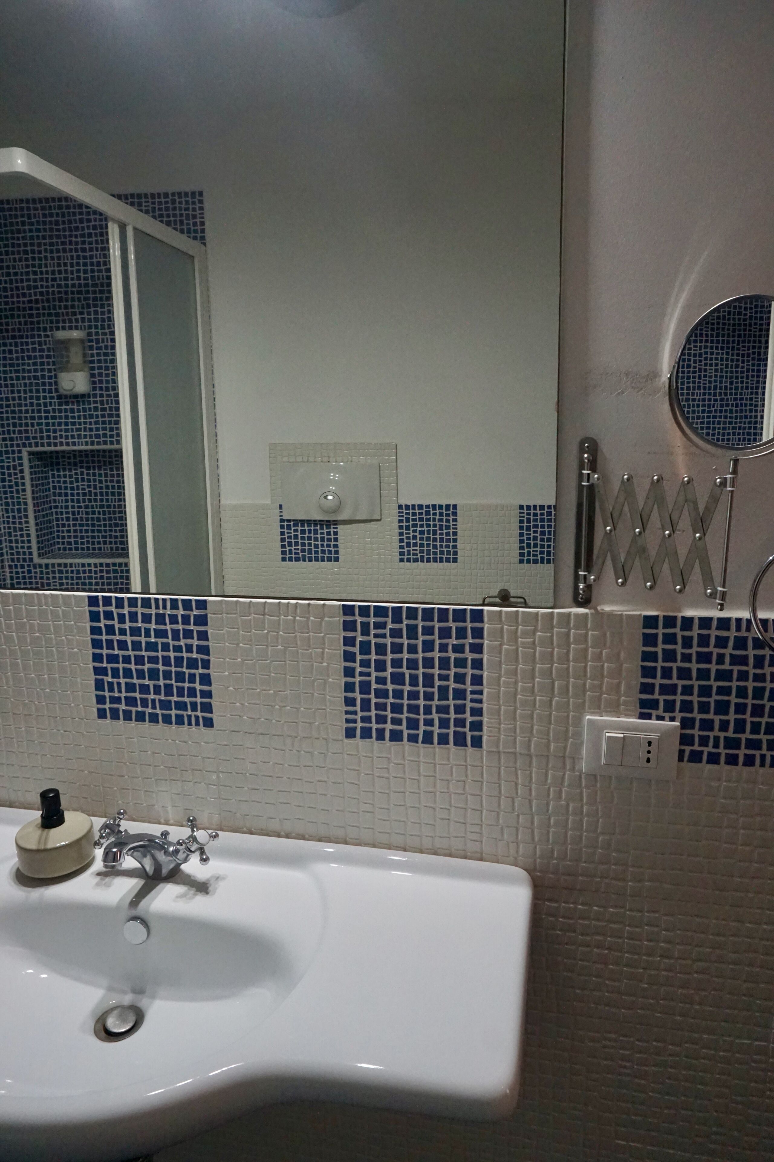 A bathroom with a white sink, blue mosaic tiles, a mirror, and a towel rack.