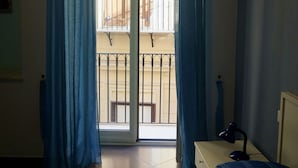 Camera da letto con un letto, un comodino, una lampada e vista su un balcone con ringhiera.