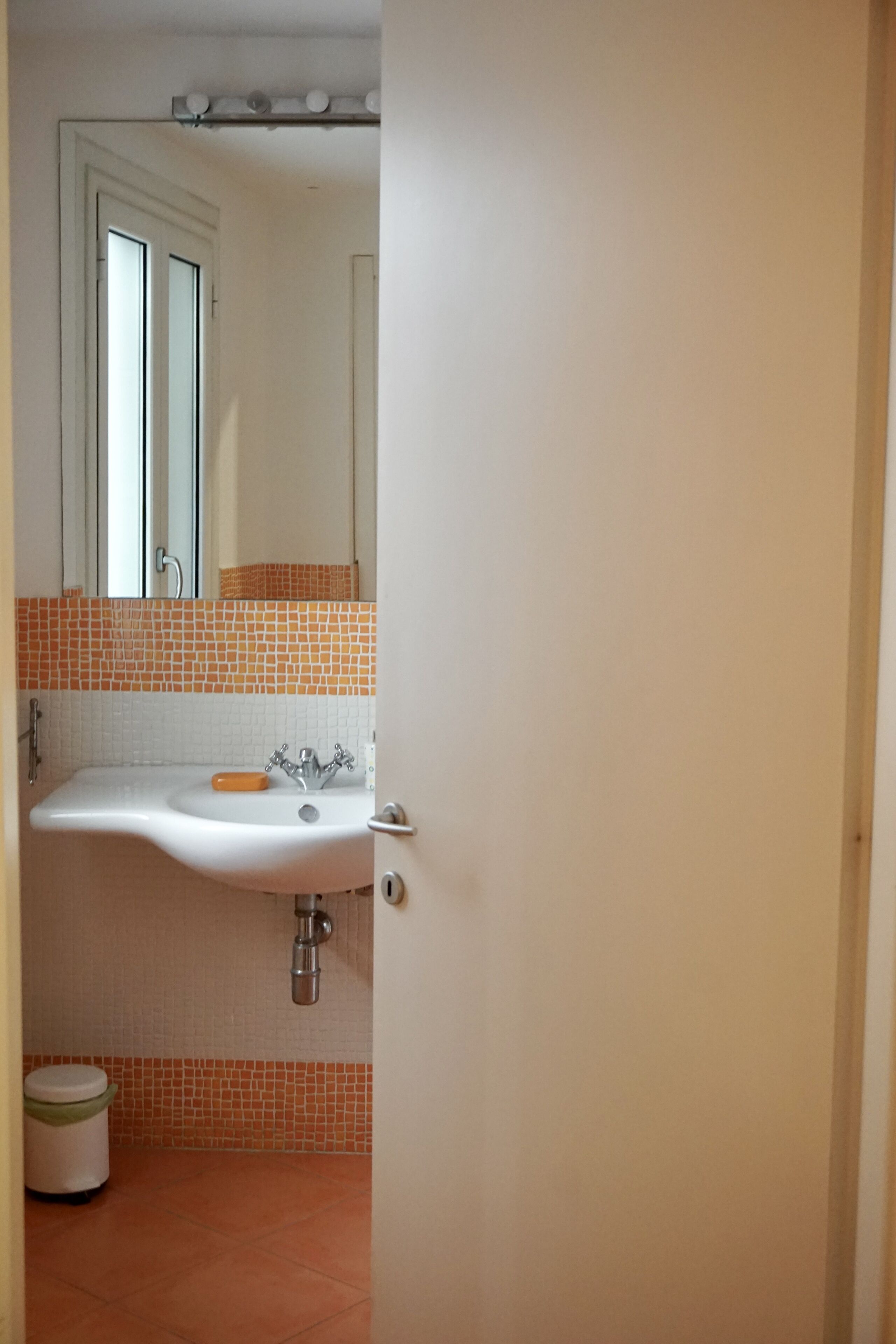 A bathroom with a white sink, orange-tiled backsplash, and a visible toilet.