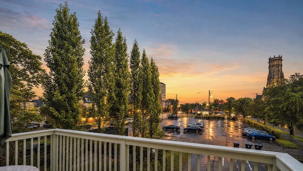 A balcony with a view of a parking lot and a tower in the distance. - Charming 3BR | Highly Walkable | Free Parking! (Louisville)