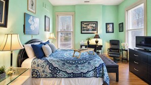 A bedroom with a bed, bedside tables, a desk, a chair, a television, and a window with blinds. - Charming 3BR | Highly Walkable | Free Parking! (Louisville)