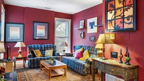 A living room with a red wall, two blue plaid sofas, a coffee table, and a large abstract painting. - Charming 3BR | Highly Walkable | Free Parking! (Louisville)
