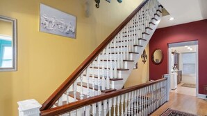 A staircase with white balusters and a wooden handrail, leading to a room with a red wall and a framed picture above the door. - Charming 3BR | Highly Walkable | Free Parking! (Louisville)
