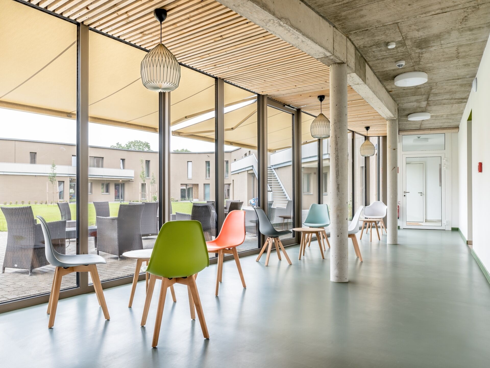 An indoor seating area with modern chairs and tables, large windows, and a concrete ceiling.