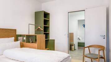 Ein modernes Schlafzimmer mit einem Bett, einem Holzstuhl, einer grünen Regaleinheit und einer Tür zu einem anderen Raum.