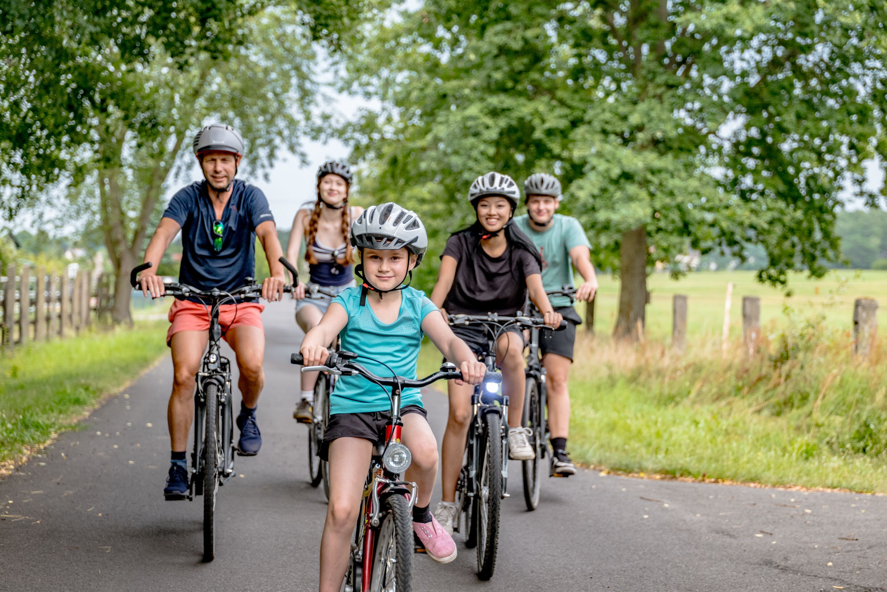 A group of people riding bicycles on a paved path surrounded by trees.